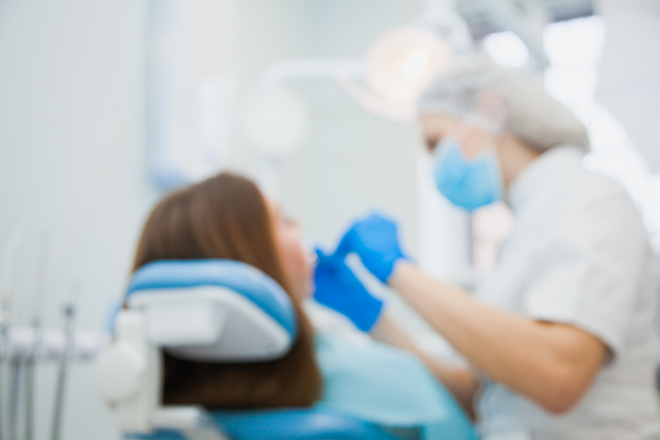 Defocused, Blurred Image Of Dentist With Patient At Clinic Office