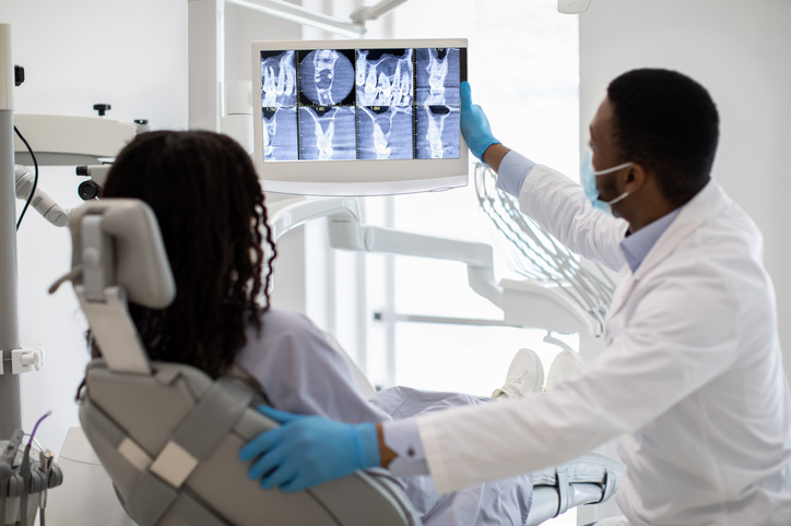 Professional Black Dentist Doctor And Female Patient Looking At Teeth Xray Picture